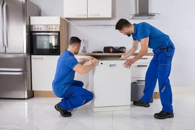 Two appliance repair technicians working together in a home kitchen