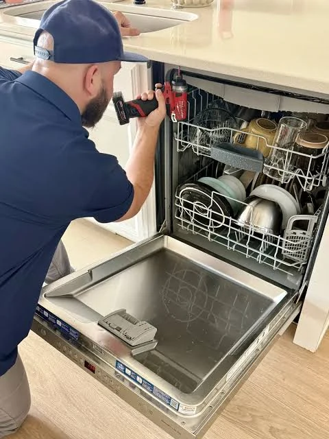 Technician inspecting a dishwasher installed under a kitchen counter
