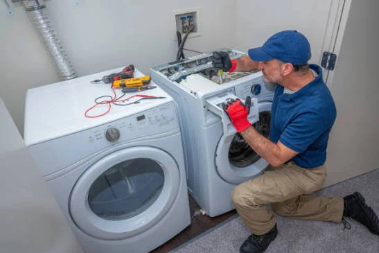 Technician working on a washer beside a clothes dryer